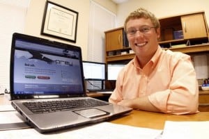 A man smiling while engaged in cyber crime on a laptop computer.