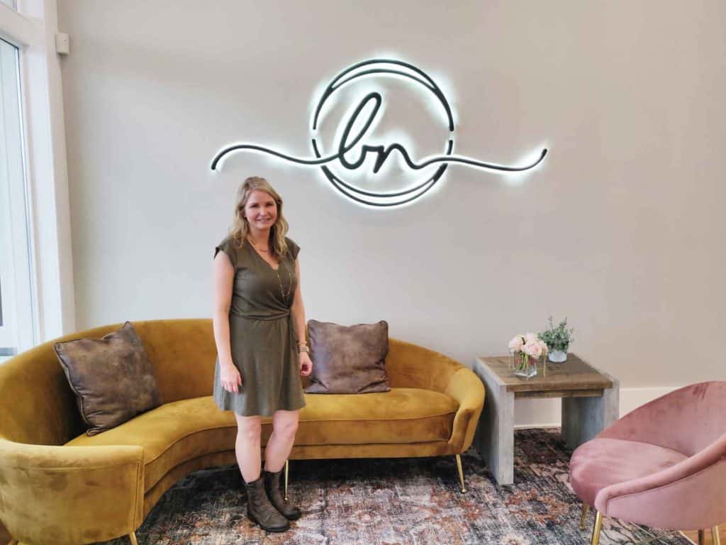 A woman standing in front of a couch with a neon sign.
