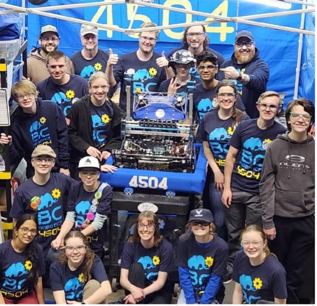 A team of robotics enthusiasts, embracing STEM Education, posing proudly with their robot at a robotics competition event.
