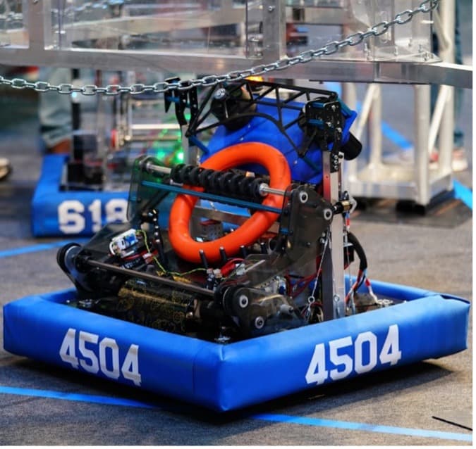 A competition robot with the number 4504, designed for STEM education, featuring a red and black ring, on a blue bumper pad enclosed by a chain barrier.