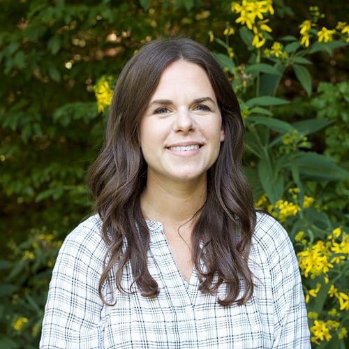 A woman in a plaid shirt standing in front of yellow flowers.